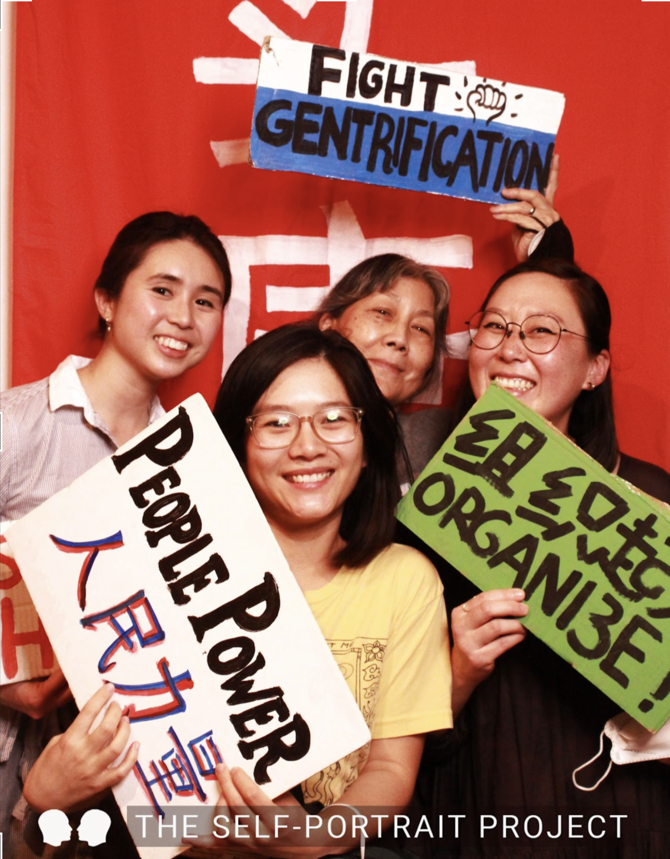 Four people stand in front of a red background holding signs that say ""People Power", "organize!", and "fight gentrification."